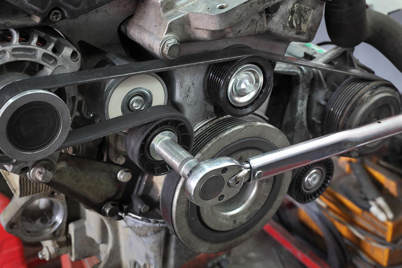 Technician installing new drive belt and tensioner pulley in engine maintenance repair